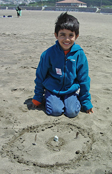 boy kneeling in sand with his artwork